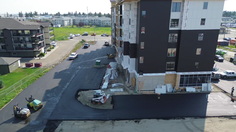 Roller finishing the completed parking lot beside a new apartment building in Olds