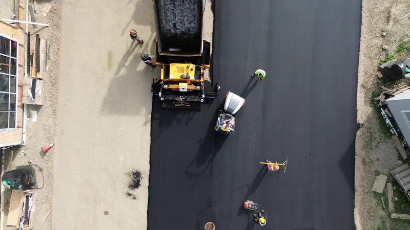 Straight-down aerial of a dump truck feeding the paver on a fresh hot mix asphalt lane