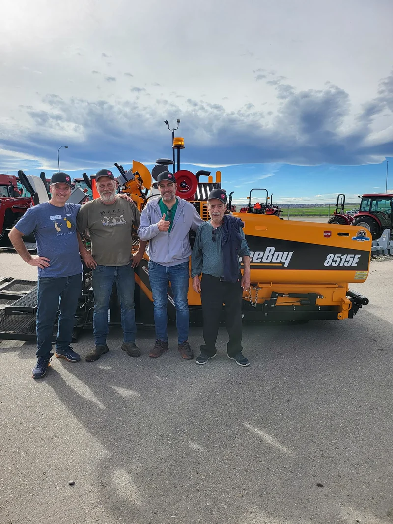 Four people standing in front of a LeeBoy 8515E asphalt paver